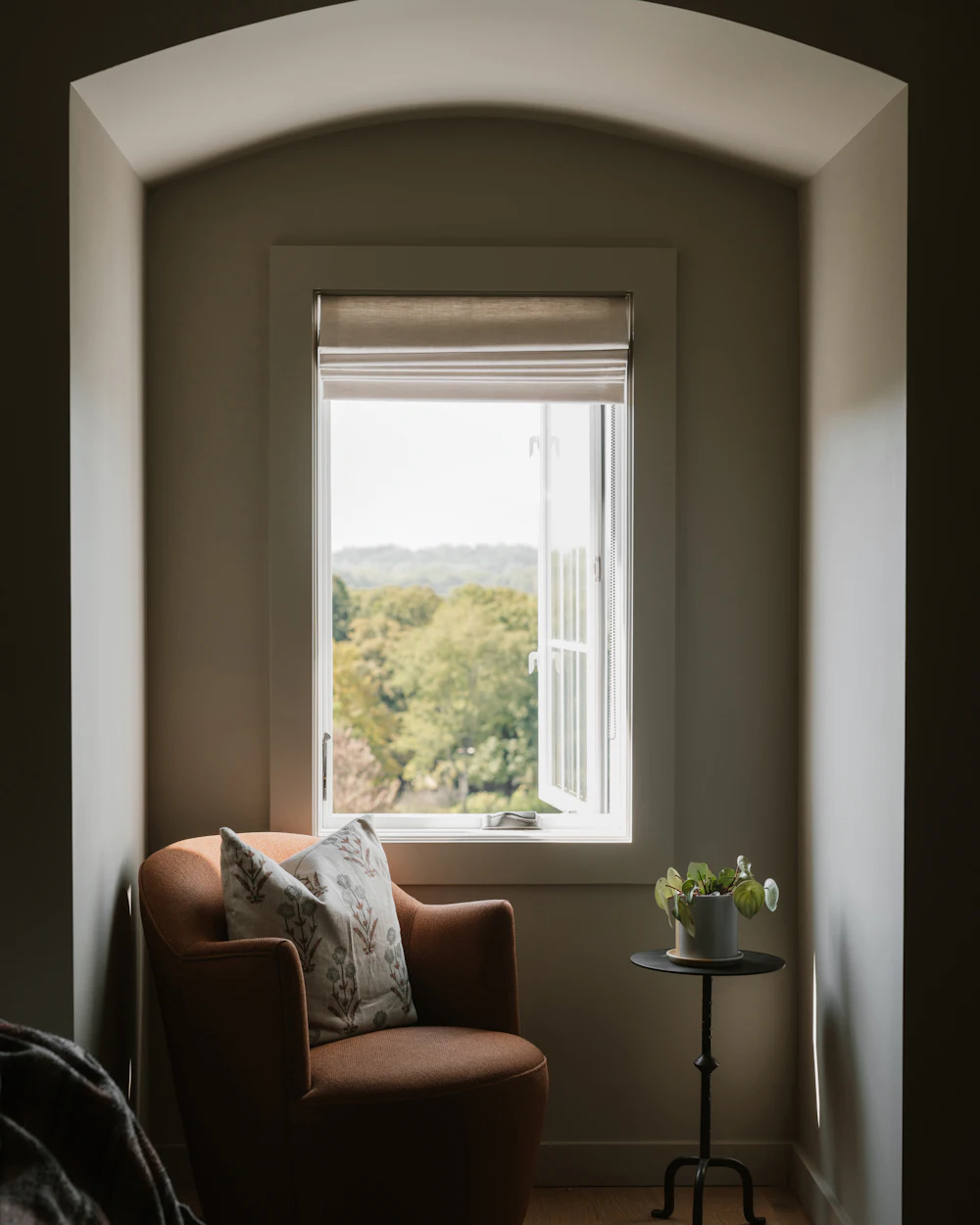 Sillón junto a una ventana con vistas a los árboles, en una sala tranquila